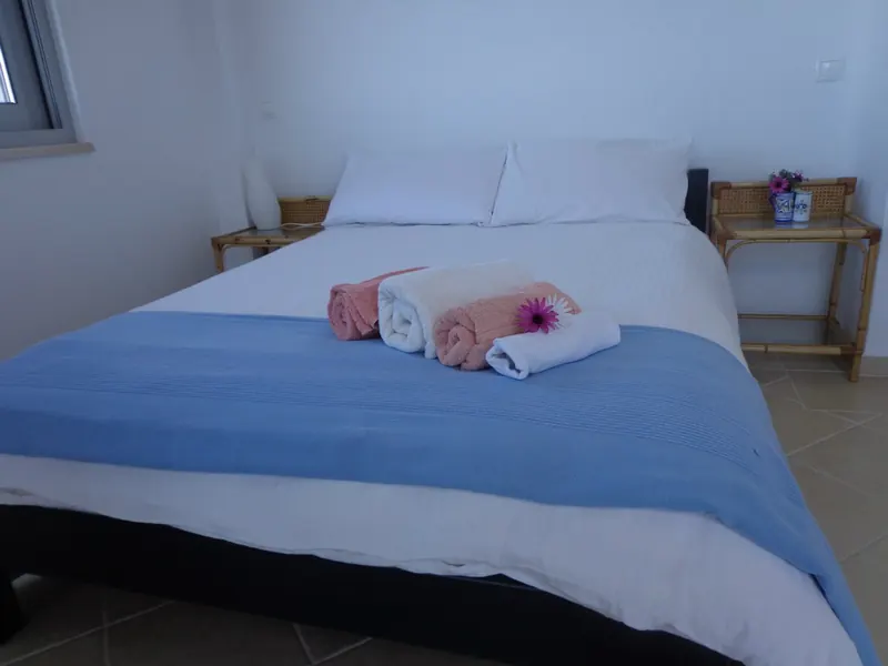 A double bed with blue cover and rolled towels in a bright guest room