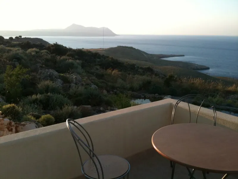 A small round table and chairs on the terrace, with the sea and coastline beyond
