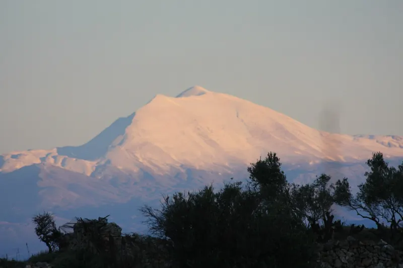 The snow-covered peak of Mount Psiloritis glowing pink at sunset